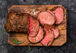Roast beef sliced with herbs and salt around the edges on a chopping board